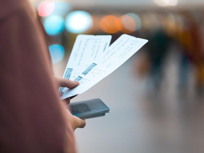A young girl is going on a trip, holds plane tickets in her hands and goes to check-in, boarding a flight, close-up view of a boarding pass on a blurred background.