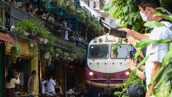 Turis mengambil foto kereta api yang melewati kawasan permukiman tua di pusat kota Hanoi, Minggu, (28/8/2022).