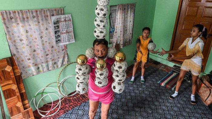 TOPSHOT - This photograph taken on July 5, 2022 shows septuagenarian Ohn Myint (C) keeping watch on a performing youth as his granddaughter Han Myint Mo (L) looks on during a juggling training session at a residence in Yangon. - Han Myint Mo kicks up a gold-coloured metal ball, pirouettes and catches it on the blade of a knife held in her teeth -- keeping up a Myanmar juggling tradition on the edge of extinction. - To go with 'MYANMAR-TRADITION-LIFESTYLE-JUGGLING,FOCUS' (Photo by AFP) / To go with 'MYANMAR-TRADITION-LIFESTYLE-JUGGLING,FOCUS' (Photo by STR/AFP via Getty Images)