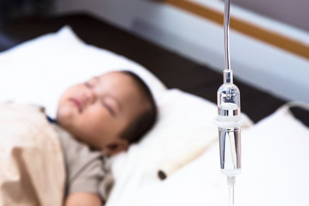 5 months old baby with dehydration, receiving medication through intravenous fluid therapy while asleep in hospital bed, focus on drip chamber