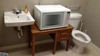 Desain toilet ini cukup aneh dan mengundang tawa. Di antara wastafel dan closet, ada meja terbentang dengan microwave yang terpasang di sana. Mungkin biar lebih praktis menghangatkan makanan ya? Foto: Site News