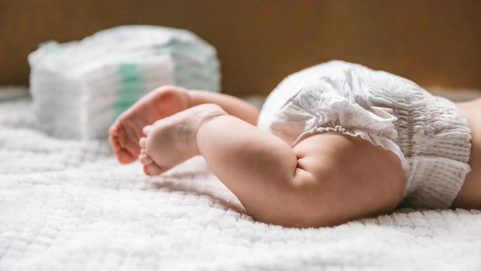 A baby in a diaper at the age of two months and a stack of diapers. How to choose baby diapers