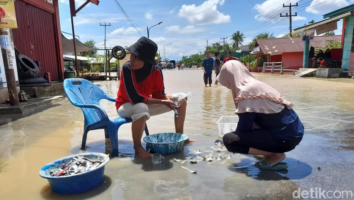 Warga mencuci alat makan di air banjir.