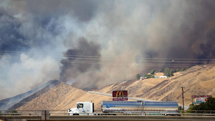 CASTAIC, CALIFORNIA - AUGUST 31: Firefighters work as a tow truck tows away the trailer of a truck while the Route Fire burns on August 31, 2022 near Castaic, California. Evacuations have been ordered as the brush fire has scorched more than 600 acres and closed down the 5 freeway amid a heat wave in Southern California. (Photo by Mario Tama/Getty Images)