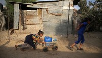 Anak-anak perempuan yang mendorong serta menarik jeriken berisikan air minum dengan gerobak kecil.