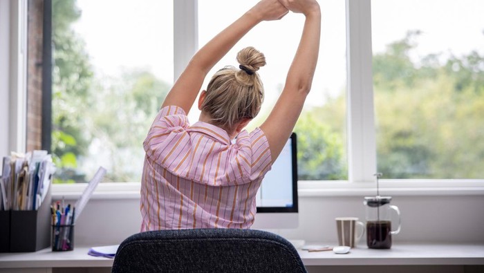 kerja seperlunya demi mental health Rear View Of Woman Working From Home On Computer In Home Office Stretching At Desk