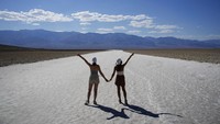 Turis berfoto dengan lanskap mematikan Death Valley. Suhu di Lembah Kematian bisa sangat ekstrem karena dipengaruhi oleh beberapa faktor. Area taman nasional ini termasuk tempat paling rendah di dunia dengan posisi 86 meter di bawah permukaan laut dan dikelilingi oleh pegunungan.    