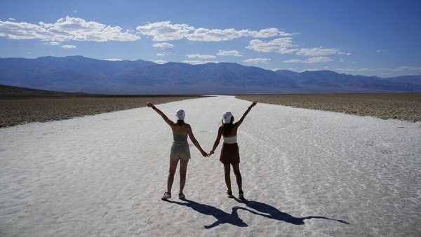 Turis berfoto dengan lanskap mematikan Death Valley. Suhu di Lembah Kematian bisa sangat ekstrem karena dipengaruhi oleh beberapa faktor. Area taman nasional ini termasuk tempat paling rendah di dunia dengan posisi 86 meter di bawah permukaan laut dan dikelilingi oleh pegunungan.    