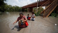 Warga yang berjalan menerobos banjir sembari membawa barang-barang mereka untuk diamankan.