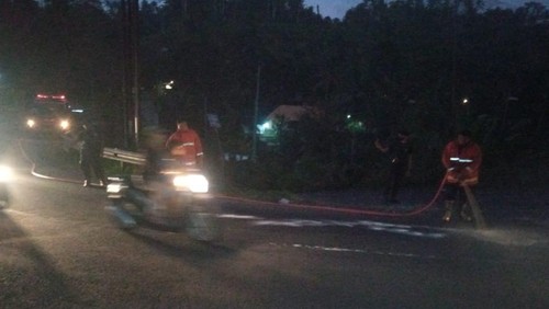 Petugas Damkartan Karangasem saat melakukan penyemprotan ceceran oli yang menyebabkan kecelakaan di jalur Rendang