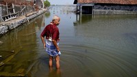Sukarman berjalan di tengah banjir di luar rumahnya, Sabtu (30/7/2022). Ia sempat berpikir bahwa dirinya harus mencoba keluar dari desa bersama cucunya. Namun, ia pasrah dengan kenyataan bahwa ia tak punya uang atau rumah keluarga lainnya. Kemungkinan, ia akan menghabiskan sisa hidupnya tinggal di rumah yang semakin banjir.