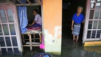 Sudarto berdiri di depan pintu dan putrinya Turiah yang duduk di atas kasur beralas kayu yang ditinggikan untuk mencegah banjir ari laut pasang (rob). Turiah mempunyai cacat fisik yang menghalanginya dari pekerjaan normal di Desa Timbulsloko, Demak, Jawa Tengah, Minggu (31/7/2022).