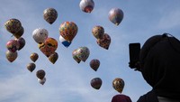 Seorang penonton mengabadikan balon udara yang tengah terbang dengan ponselnya.