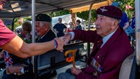 Peserta menyemangati para veteran Inggris Perang Dunia II dan bersalaman saat veteran tersebut lewat menggunakan mobil.