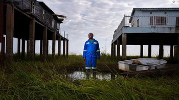 Jasper Doest mengabadikan Lubinda Lubinda, manajer stasiun untuk Otoritas Sungai Zambezi yang berdiri di depan rumah lamanya (kiri) dan rumah barunya (kanan). Kekeringan yang sering terjadi di sepanjang Sungai Zambezi. Foto: Wildlife Photographer of the Year