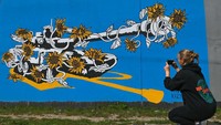 Warga memotret mural bergambar tank yang diselimuti bunga matahari.