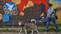 Perempuan ditemani anjingnya melintas di depan mural pada tembok Stasiun Kereta Gdask Jasie, Polandia, Senin (5/9/2022). Sebanyak 25 mural bertema anti perang dilukis di sini.