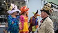 Orang-orang terlihat menikmati Festival Topi Bridport dengan salah seorang peserta memakai topi aneka wajah.
