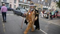 Seorang pria berpakaian seperti raja singa melintasi jalan di Festival Topi Bridport. Selain hiasan topi yang unik dan elegan, tak jarang juga peserta yang datang dengan hiasan yang aneh.