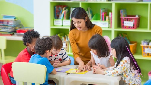 Asian female teacher teaching mixed race kids reading book in classroom,Kindergarten pre school concept