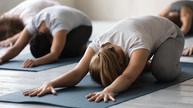 Group of people lying on mats performing Child Pose close up focus on caucasian woman. Participants beginners rest after work out in sport club studio, reduces stress and fatigue, yoga session concept