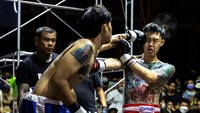 Seorang petarung mendaratkan pukulan ke wajah lawannya. Aksi-aksi ini menjadi daya tarik penonton yang memadati kuil tempat pertandingan berlangsung.