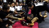 Seorang petarung jatuh ke matras. Penonton yang berada sangat dekat dengan arena pertarungan membuat semakin panas suasana.