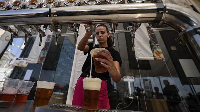 Seruput Taybeh, Bir Halal dari Palestina TOPSHOT - A bartender serves visitors on September 2, 2022, during the annual annual Oktoberfest beer festival in the village of Taybeh in the village of Taybeh, east of the occupied West Bank city of Ramallah, home of the Palestinian Taybeh brewery founded in 1994. - Ever since 2005, the Taybeh brewery has been brewing beer under challenging circumstances. Now the brewery is run by a woman, Madees Khoury, adding an extra layer of complication. Run as a two-day weekend event, Oktoberfest at Taybeh is as much about Palestinian identity as it is about drinking beer. (Photo by Abbas MOMANI / AFP) (Photo by ABBAS MOMANI/AFP via Getty Images)