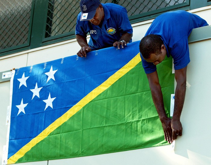 National Peace Council workers display the Solomon Islands national flag outside their office in Honiara, 26 July 2003, before destroying illegal weapons as part of the amnesty offered to the various warring militias.  Over 2,200 troops and police from Australia, New Zealand, Fiji, Papua New Guinea and Tonga are taking part in Operation Helpem Fren to restore law and order to the deeply troubled South Pacific nation.  AFP PHOTO/Torsten BLACKWOOD (Photo by TORSTEN BLACKWOOD / AFP)