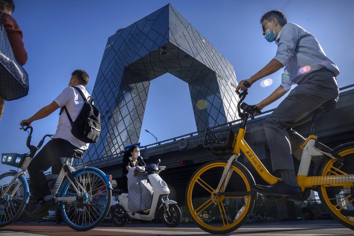 Commuters wearing face masks ride bicycles near the China Central Television (CCTV) building in the central business district in Beijing, Thursday, Sept. 1, 2022. (AP Photo/Mark Schiefelbein)