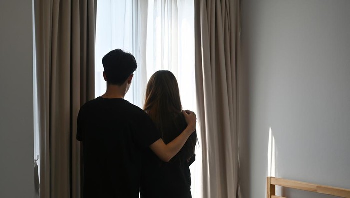 A portrait of a couple standing on a bedroom together, a man wrapping his hand on the womans shoulder, for marriage life, relationship and family life concept.