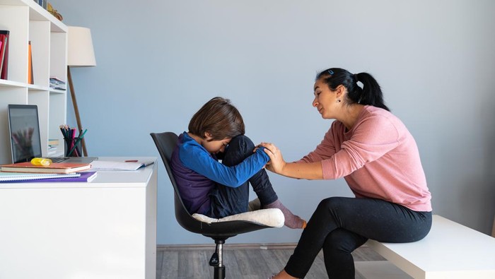 Photo of mother talking to her bored schoolboy son having online education during Coronavirus pandemic quarantine. Mother has black hair and is asian. Shot indoor with a full frame mirrorless camera.