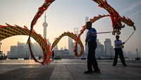 Pria memutar pita naga di kawasan pejalan kaki Bund di sepanjang Sungai Huangpu saat matahari terbit di Shanghai.