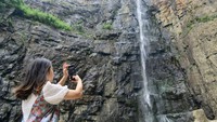 Seorang wanita mengabadikan air terjun dengan ponsel pribadinya.