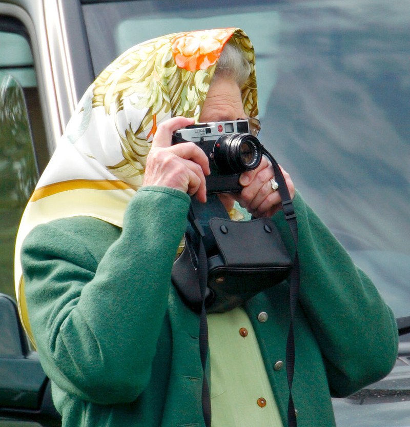 British Royal Queen Elizabeth II, wearing a headscarf and a waxed jacket, takes a picture with her Leica M6 camera at the Royal Windsor Horse Show, held at Windsor Home Park in Windsor, Berkshire, England, 12th May 1989. (Photo by Tim Graham Photo Library via Getty Images)