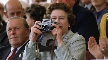 Ratu Inggris, Queen Elizabeth II asik memotret di antara kursi VVIP saat saat menonton kejuaraan Royal Windsor Horse Show, 16 Mei 1982.
