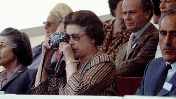 Ratu Inggris, Queen Elizabeth II terekam sedang asik memotret saat menonton kejuaraan Royal Windsor Horse Show, 16 Mei 1982. (Tim Graham Photo Library/Getty Images)