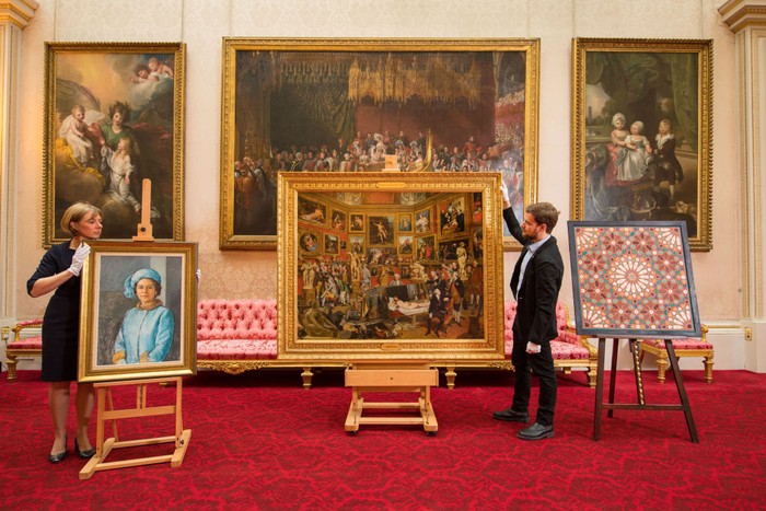 Royal Collection staff adjust (front row, left to right) an oil sketch 'HM the Queen, 1972-73' by Michael Noakes, 'The Tribuna of the Uffizi, 1772-77' and a Moroccan inspired painting by Natasha Mann during the press preview of the Prince and Patron exhibition at Buckingham Palace, London, which will mark the 70th birthday of the Prince of Wales this year. (Photo by Dominic Lipinski/PA Images via Getty Images)