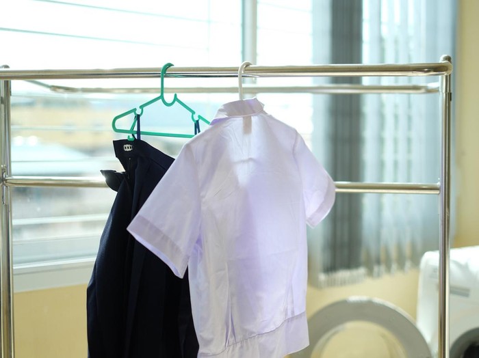 Student uniforms after washing hang on the clothes line. White shirts and blue skirts drying on clothes rack inside the house. Back to school concept.