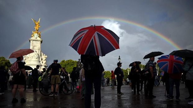 A person with an Union flag-themed umbrella shelters from the rain by the Queen Victoria Memorial opposite Buckingham Palace, central London, on September 8, 2022. - Queen Elizabeth II, the longest-serving monarch in British history and an icon instantly recognisable to billions of people around the world, has died aged 96, Buckingham Palace said on Thursday. (Photo by Daniel LEAL / AFP)