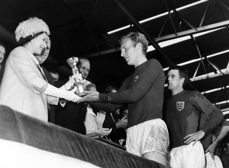 Britain's Queen Elizabeth of England presents the Jules Rimet Cup to Bobby Moore, captain of England's national soccer team, as her husband Prince Philip (C) and forward Geoff Hurst (R) look on after England beat West Germany 4-2 in extra time in the World Cup final 30 July 1966 at Wembley stadium in London. - Hurst scored three goals, two of them in extra time, to help England win its first World title. (Photo by - / AFP) (Photo by -/AFP via Getty Images)