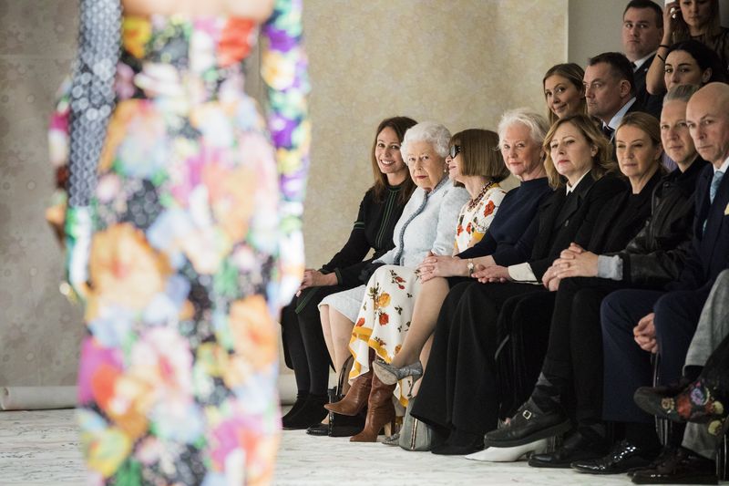 LONDON, ENGLAND - FEBRUARY 20:  Queen Elizabeth II (L), Chief Executive of the British Fashion Council Caroline Rush (C) and Anna Wintour (R) watch model Adwoa Aboah walking the runway at the Richard Quinn show during London Fashion Week February 2018 on February 20, 2018 in London, England.  (Photo by Tristan Fewings/BFC/Getty Images)