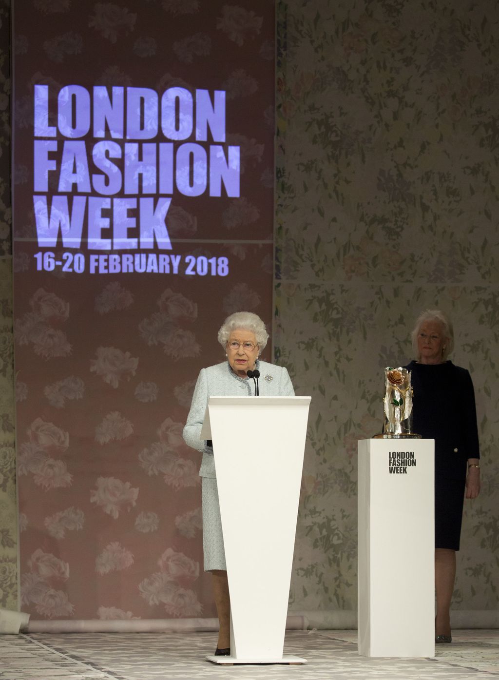 Queen Elizabeth II delivers a speech, watched by Angela Kelly, before presenting the inaugural Queen Elizabeth II Award for British Design to Richard Quinn following his Autumn/Winter 2018 London Fashion Week show at BFC Showspace, London. PRESS ASSOCIATION. Picture date: Tuesday February 20, 2018. Photo credit should read: Isabel Infantes/PA Wire (Photo by Isabel Infantes/PA Images via Getty Images)