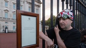 Seorang warga Inggris menelepon di depan istana sembari membaca pengumuman tentang Ratu Elizabeth II wafat. Foto: Getty Images