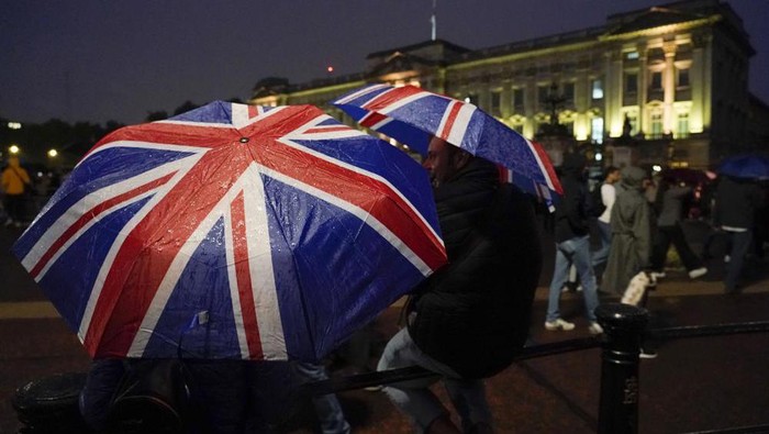 Two people walk with Union flag umbrellas as they stand in front of Buckingham Palace, after the announcement of the death of Queen Elizabeth II, in London, Thursday, Sept. 8, 2022. Queen Elizabeth II, Britains longest-reigning monarch and a rock of stability across much of a turbulent century, died Thursday after 70 years on the throne. She was 96. (AP Photo/Alberto Pezzali)