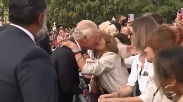 El rey Carlos III es besado por una mujer mientras saluda a los residentes en el Palacio de Buckingham.