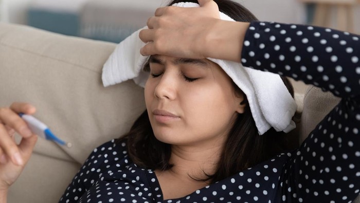 demam Unhealthy young korean asian woman measuring body temperature with electronic thermometer, applying wet towel compress to forehead relieving strong headache, seasonal contagious grippe illness concept