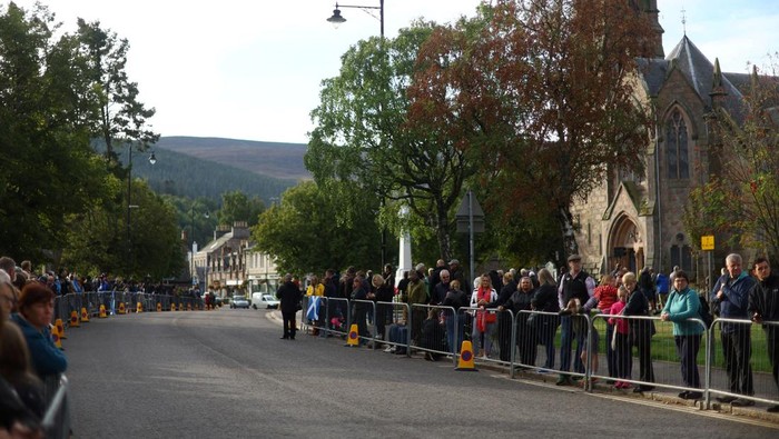 Ribuan Warga Berbaris Menanti Iring-iringan Jenazah Ratu Elizabeth II Members of the public line the streets in Ballater, as the hearse carrying the coffin of Queen Elizabeth II, will pass through Ballater, as it continues its journey to Edinburgh from Balmoral, Sunday Sept. 11, 2022. (Andrew Milligan/PA via AP)