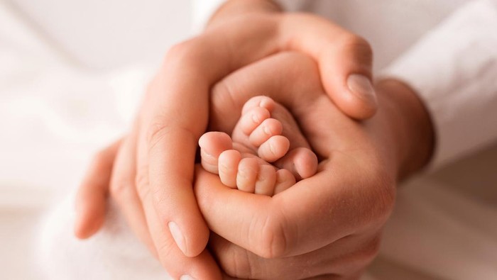 The father holds the bare feet of the newborn on a white background. Tiny legs in the hands of a man. Family, parents and homework concept. Health care, pediatrics. Black and white photography.. High quality photo