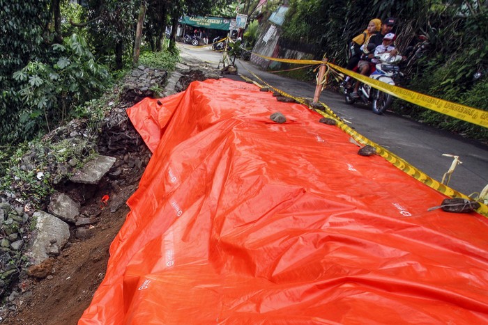 Pengendara sepeda motor melintas di dekat jalan alternatif Cilebut yang longsor di Bogor, Jawa Barat, Senin (12/9/2022). Jalan alternatif penghubung Kota Bogor dan Kabupaten Bogor itu longsor dan menghancurkan separuh jalan yang diakibatkan oleh tingginya curah hujan pada Minggu (11/9/2022). ANTARA FOTO/Yulius Satria Wijaya/aww.